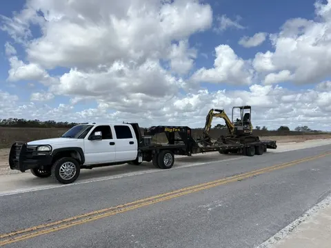 Work truck towing a compact excavator on a gooseneck trailer