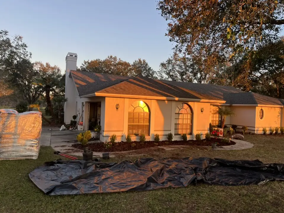 New front beds along a stucco home at sunset, with landscape fabric rolled out on the lawn and a pallet of mulch