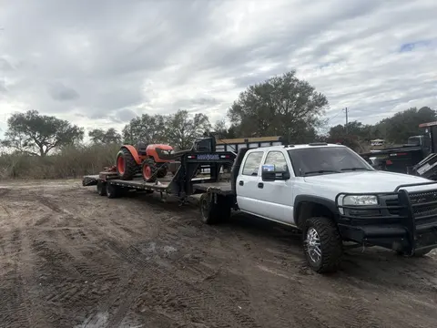Work truck towing a gooseneck trailer loaded with a tractor on a dirt job site